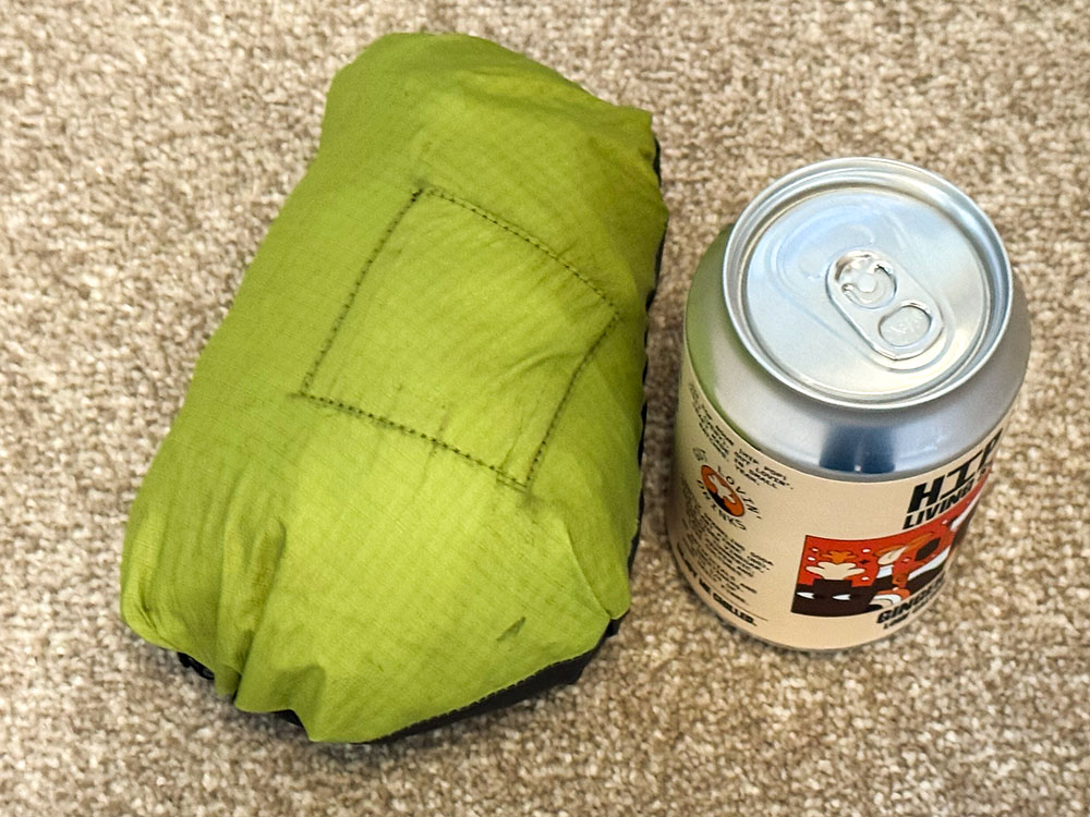 Waterproof jacket in its stuff pocket with the zip closed, next to a can showing the small packed size