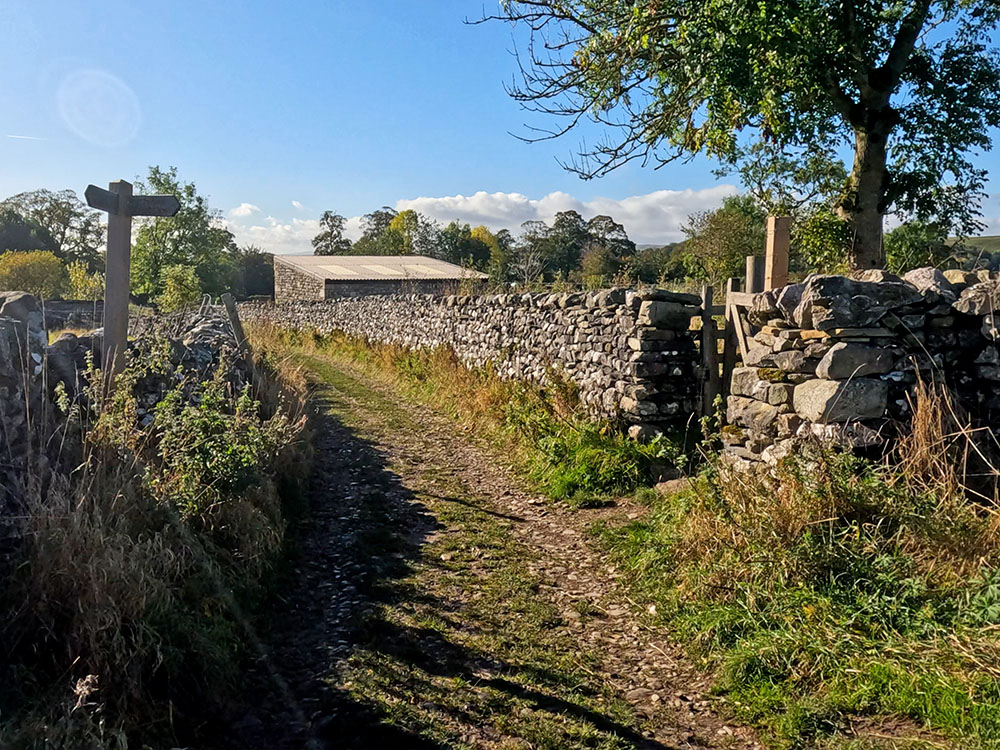 Approaching the building, footpath sign and gate in the wall