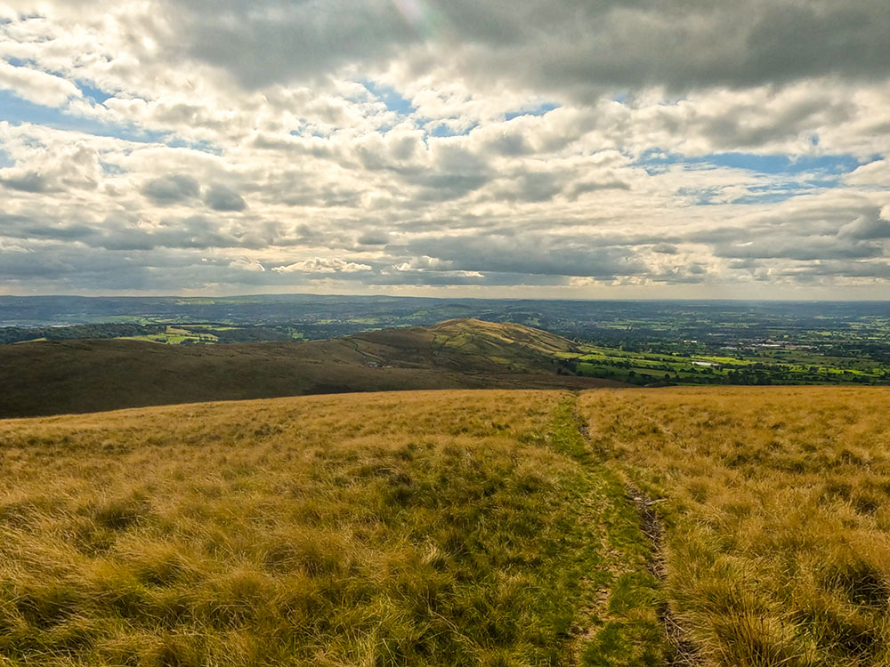 The grassy path starts to descend, with the Wellsprings ahead in the distance