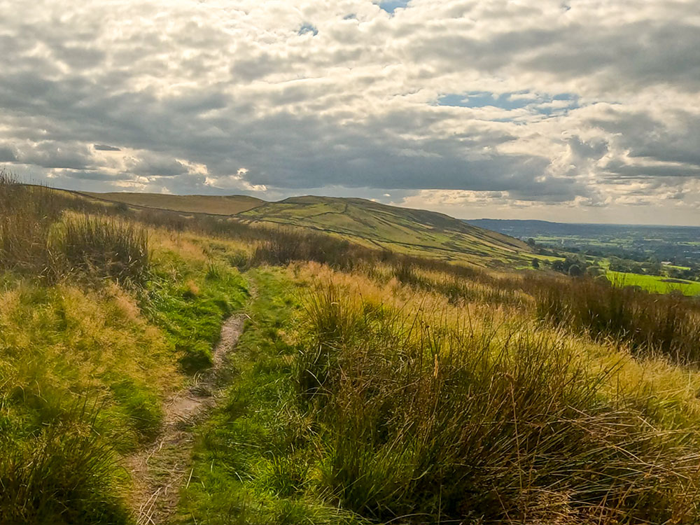 The path heads in the direction of the road and the small hills on the Nick of Pendle