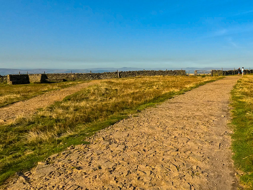 The path reaches a wall with some seats to the left and a gate straight ahead